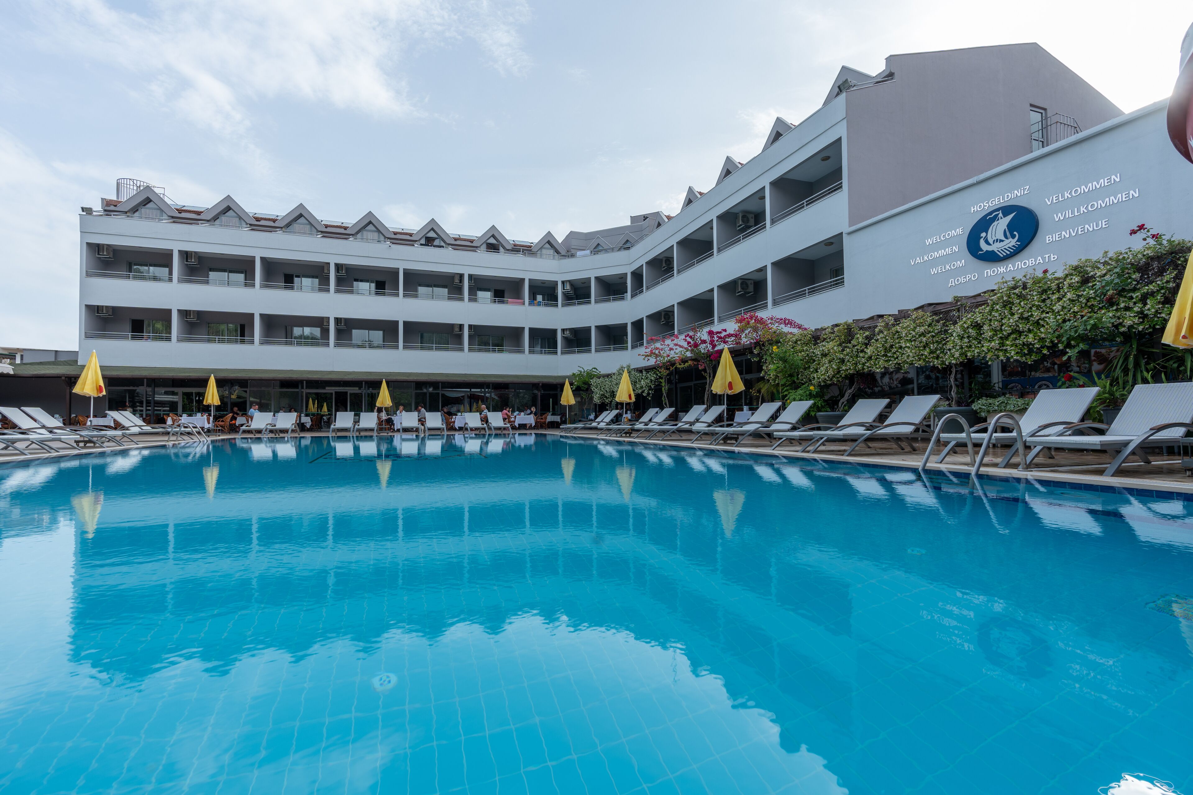 A hotel with a pool, multiple balconies, and yellow umbrellas.