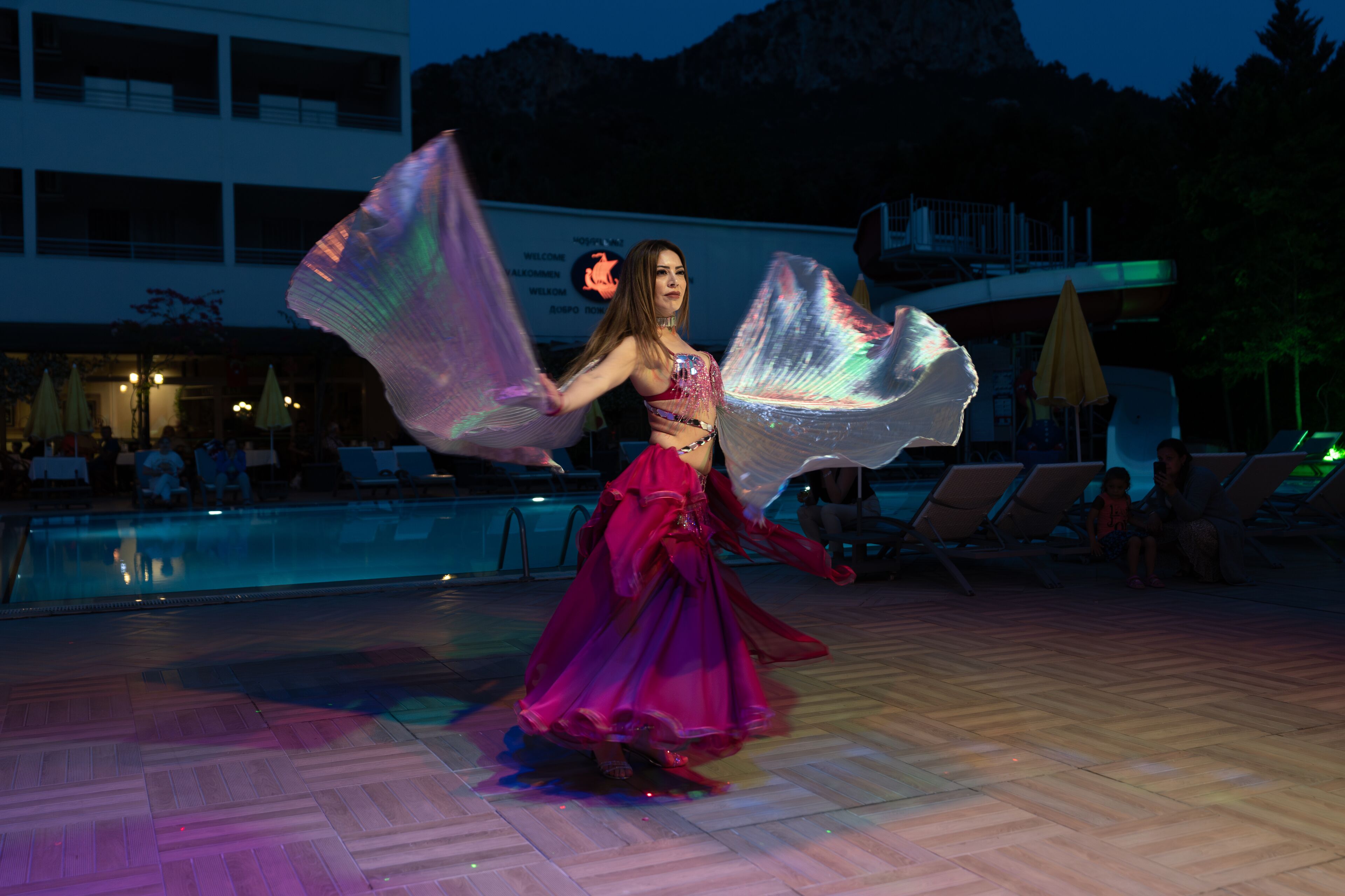A person performing with a flowing fabric near a pool area with lounge chairs and umbrellas.