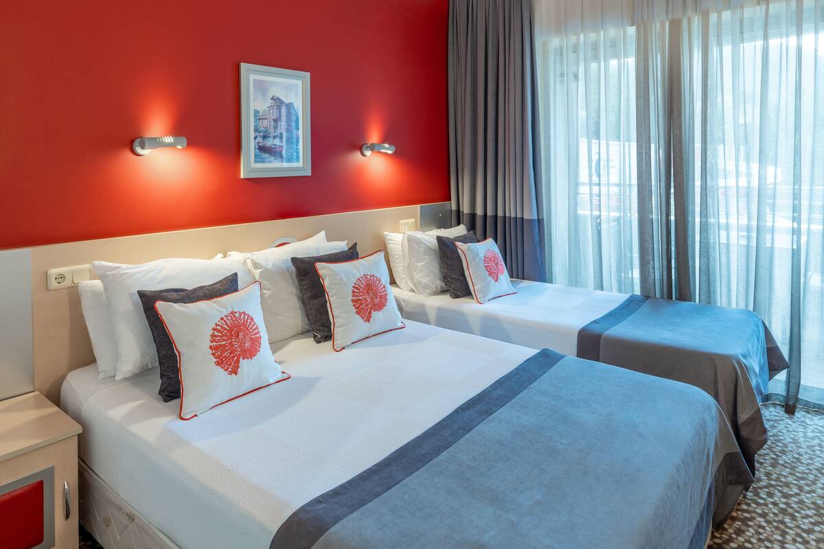 A hotel room with two beds, red walls, and a window with curtains.