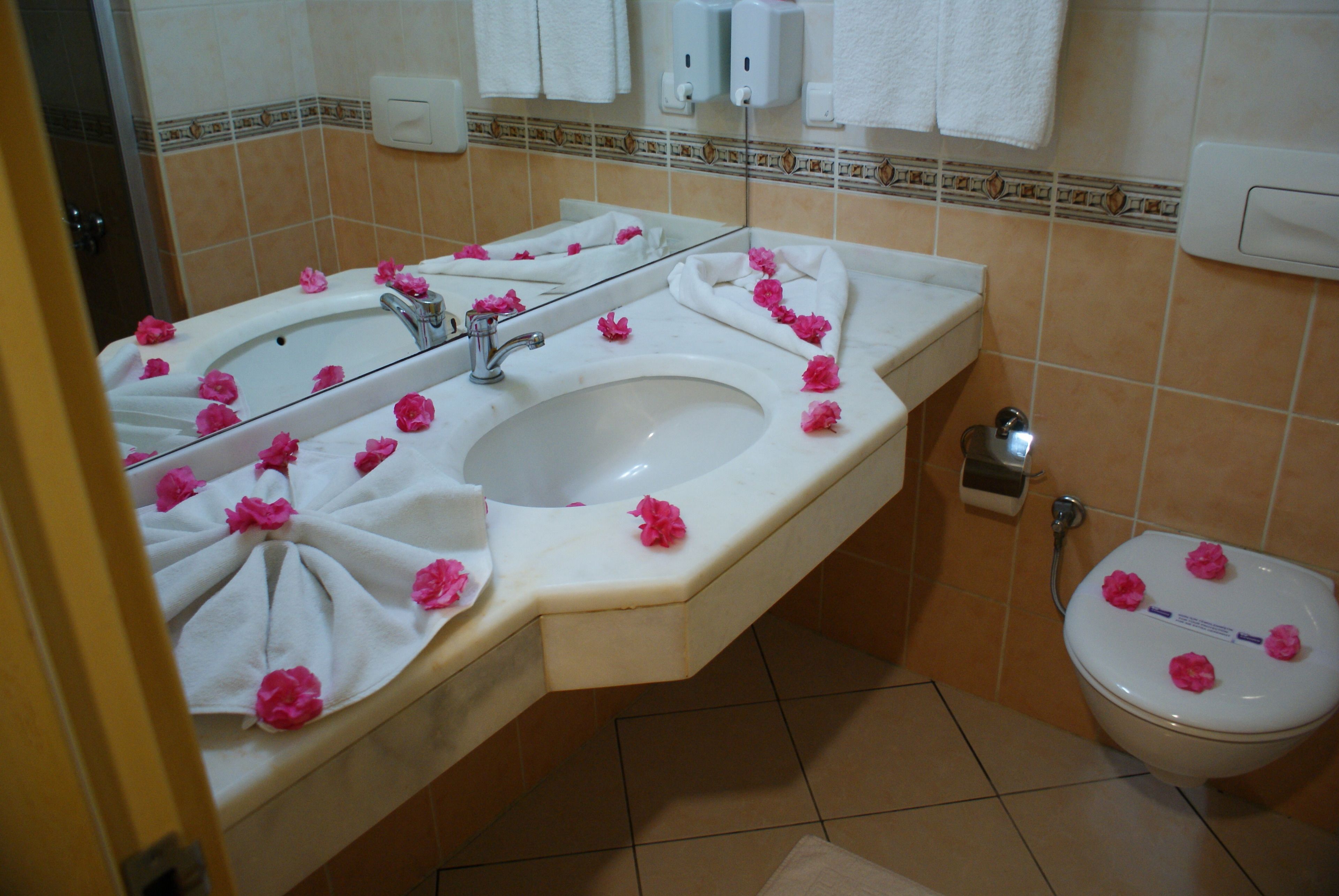 A bathroom with a sink, mirror, and toilet, decorated with pink flowers.