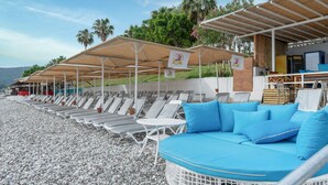 Un área de descanso junto a la playa con tumbonas y una zona de estar con cojines azules.