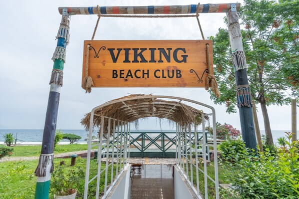 Un cartello di legno con la scritta "VIKING BEACH CLUB" e una struttura a tetto di paglia in primo piano.