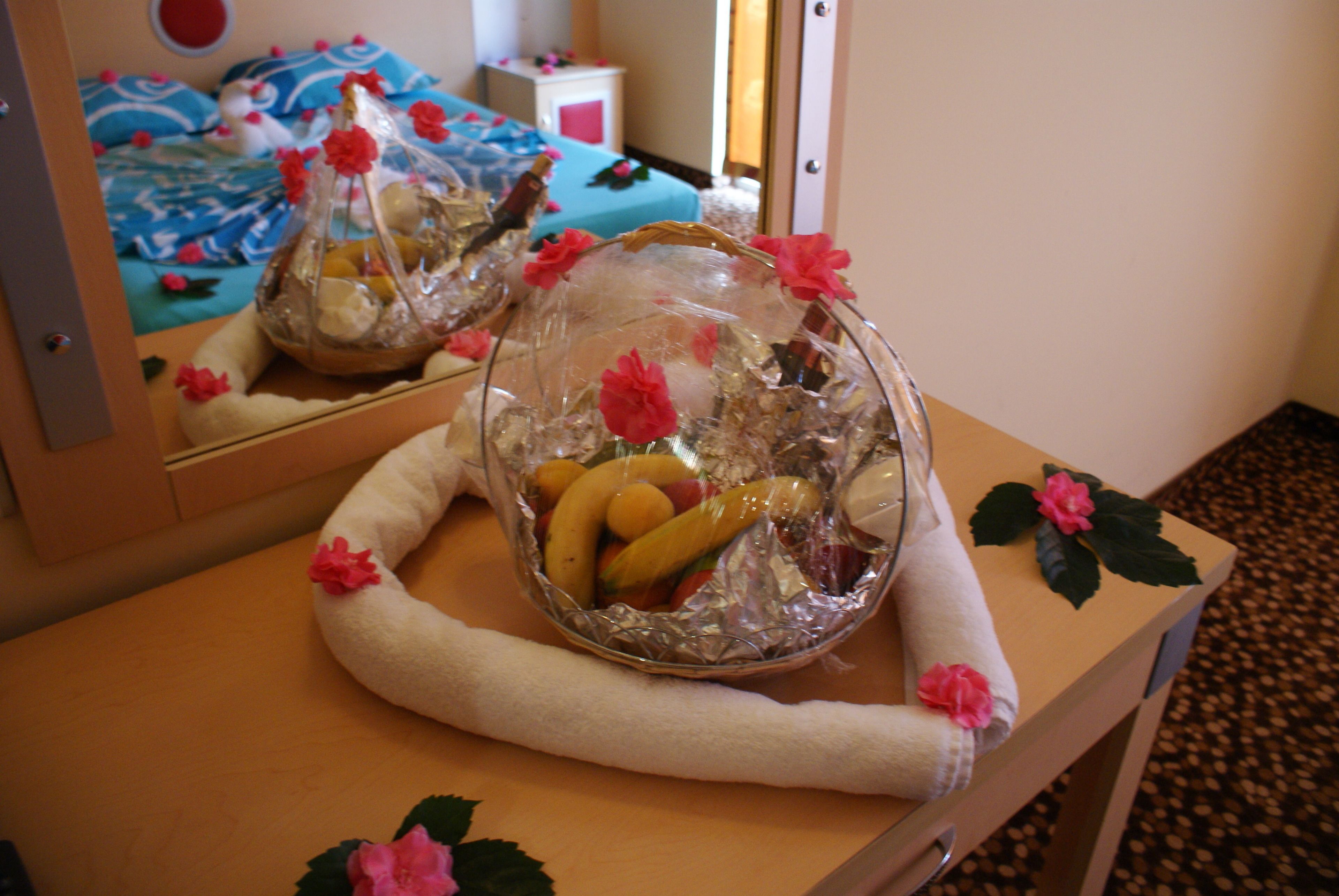 Ein Zimmer mit einem Bett, einem Nachttisch mit einer dekorativen Schale mit Früchten und Blumen sowie einem Spiegel, der den Raum reflektiert.