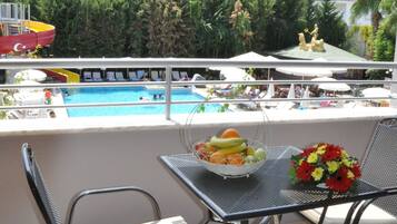 A balcony with a pool view, a table with fruit and flowers, and chairs.