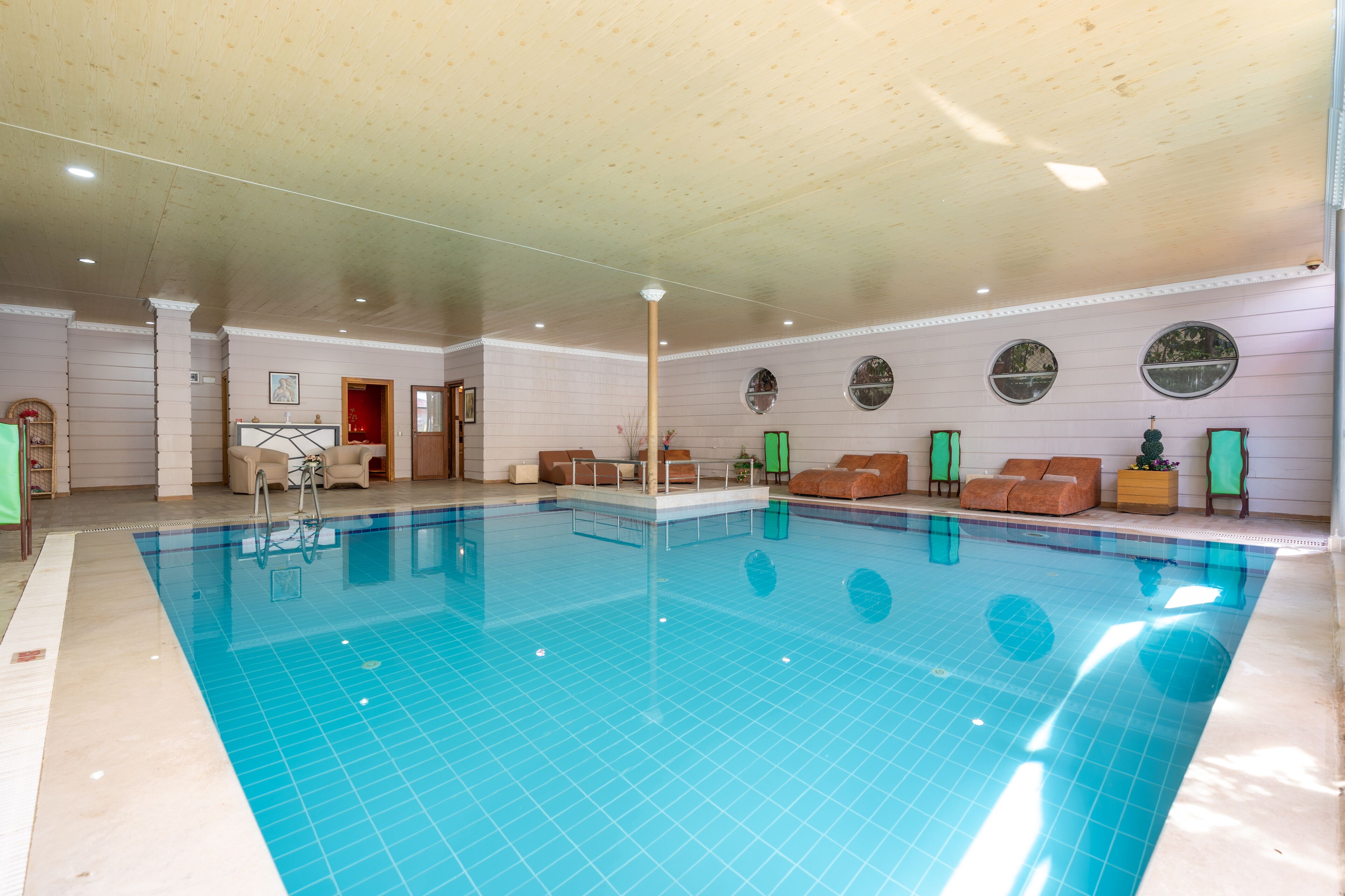 Ein Hallenbad mit gefliestem Boden, Liegestühlen und einem Empfangsbereich mit Schreibtisch und Sitzgelegenheiten.