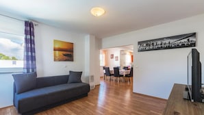 Ein Wohnzimmer mit einer Couch, einem Essbereich mit Tisch und Stühlen, einem Stadtbildgemälde und einem Fernseher.