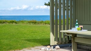 A wooden deck with a table set for a meal, overlooking a grassy area and the ocean.