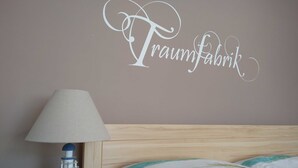 A bedroom with a bed, a nightstand, a lamp, and a wall with the text "Traumfabrik".