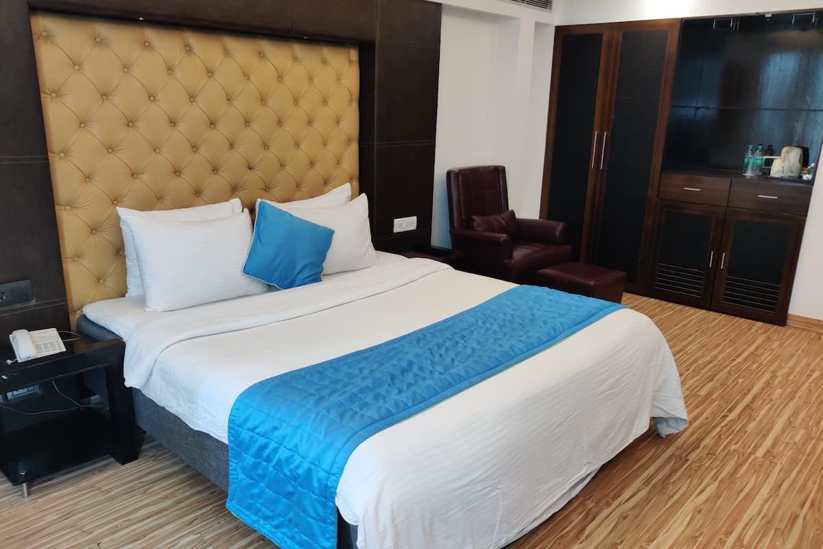 A hotel room with a large bed, a wooden floor, a brown leather chair, and a wardrobe with a mirror.