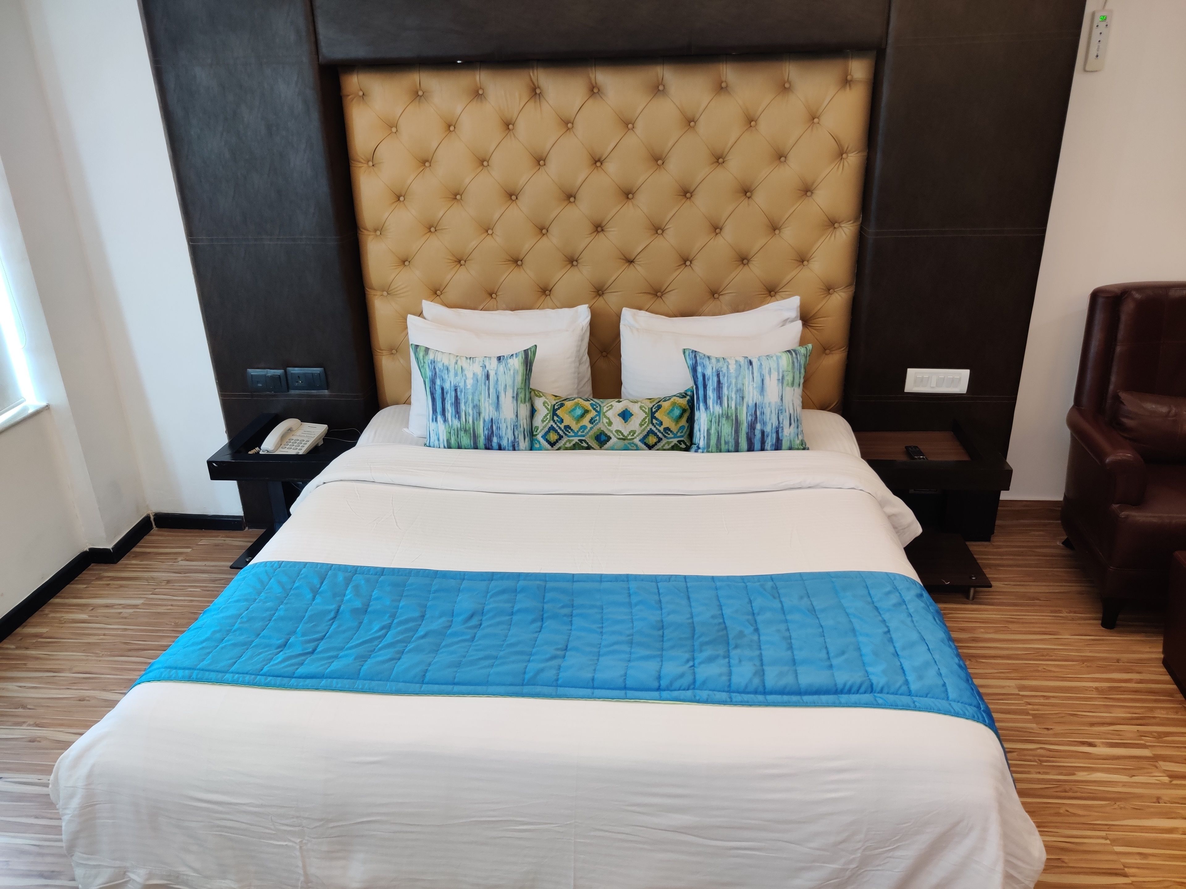 A hotel room with a large bed, a headboard, a bedside table with a phone, a chair, and a window.