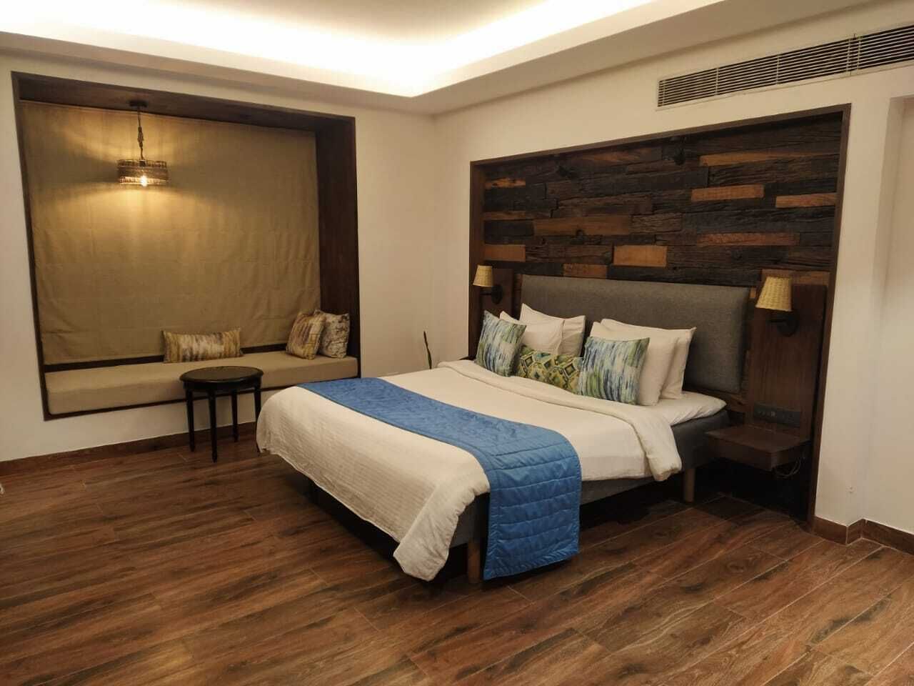 A bedroom with a large bed, a small table, a sofa, and a large window.