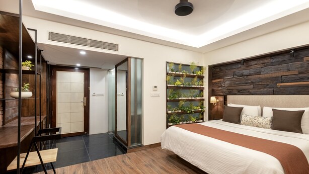 A modern hotel room with a large bed, a wooden headboard, a built-in plant wall, and a desk with a chair.