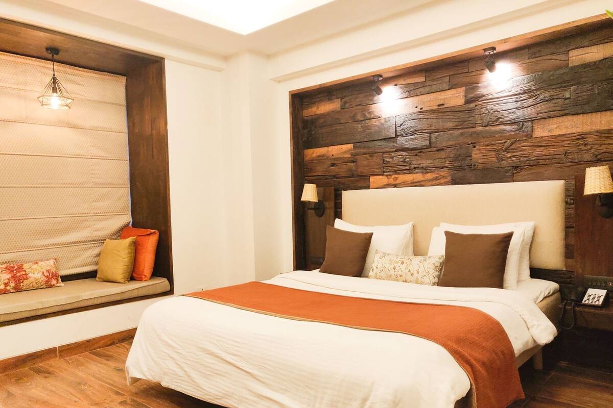 A bedroom with a bed, a bench with cushions, a wooden wall panel, and a ceiling light fixture.