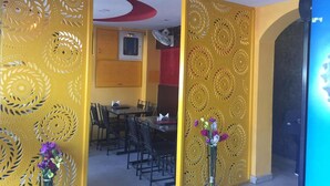 A room with yellow patterned walls, a dining area with a table and chairs, and a blue screen on the right. - Kathmandu Airport Hotel (Kathmandu)