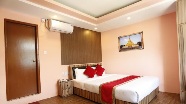 A hotel room with a wooden bed, a nightstand, an air conditioning unit, and a wall-mounted picture. - Kathmandu Airport Hotel (Kathmandu)