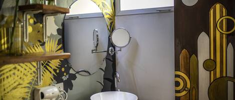 A bathroom with a white sink, a mirror, a hairdryer, and decorative wall art.