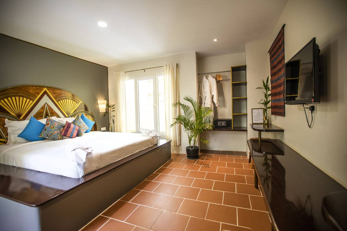 A hotel room with a bed, a potted plant, a TV, and a bathroom area.