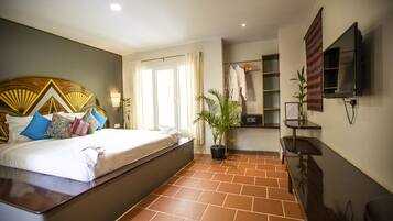 A hotel room with a bed, a potted plant, a TV, and a bathroom area.
