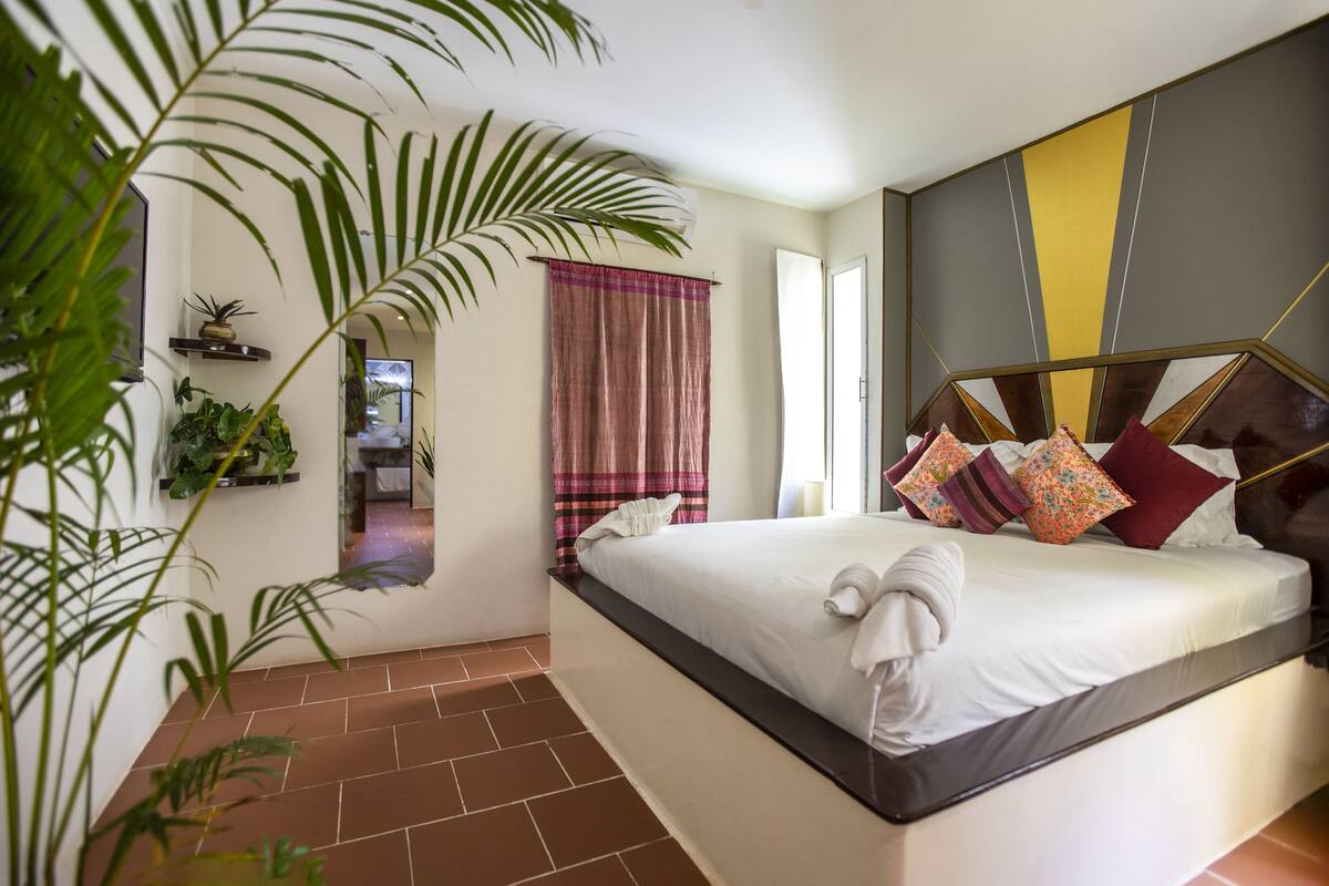 A bedroom with a large bed, a view of the hallway, and a potted plant.