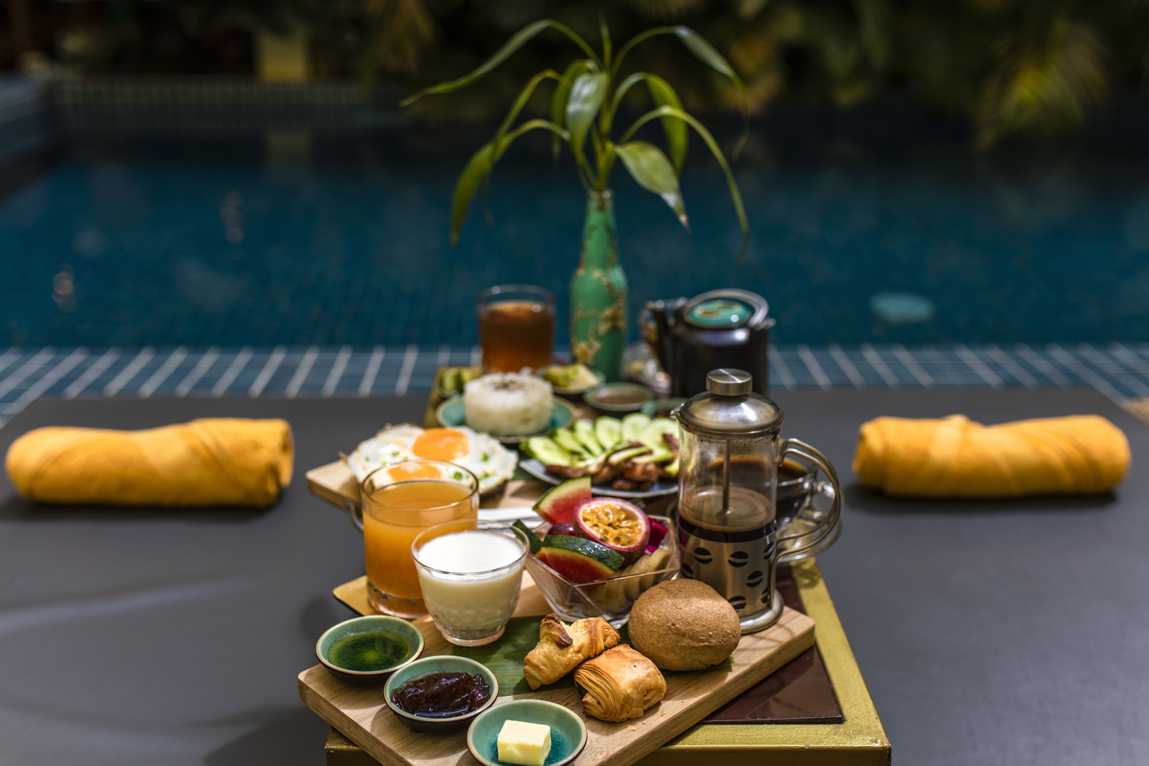 A breakfast tray with various foods and drinks by a poolside.