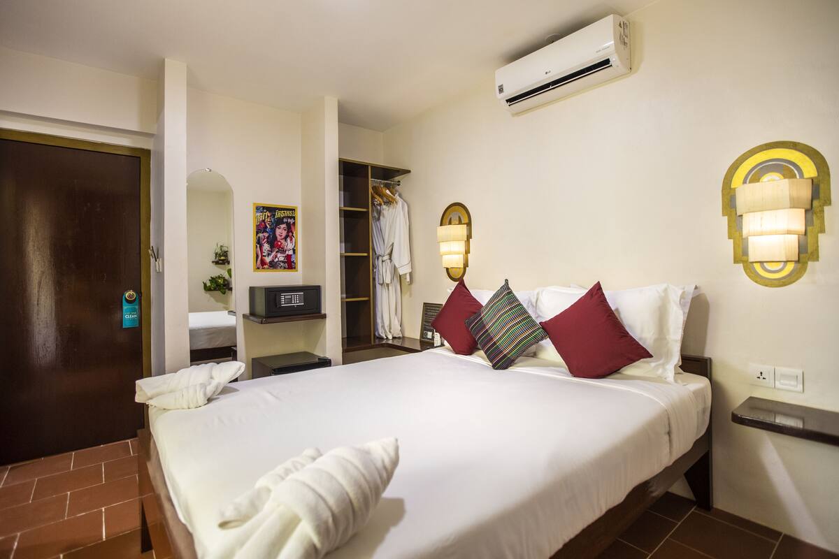 A hotel room with a bed, a wardrobe, an air conditioner, and a wall-mounted light fixture.