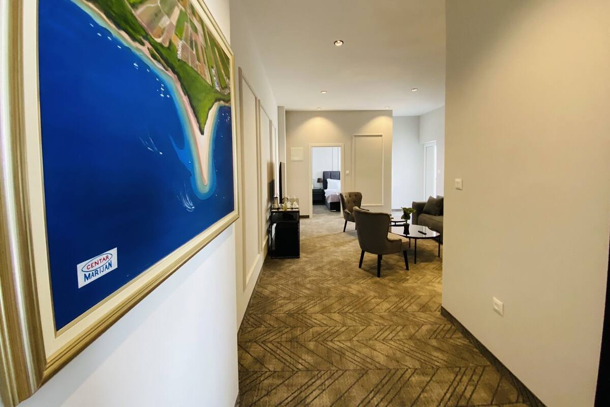 Un couloir d’hôtel avec une grande peinture abstraite sur le mur de gauche, un coin salon avec un canapé et des fauteuils, et un lit en arrière-plan.