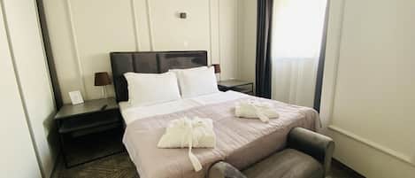 Una habitación de hotel con una cama, mesitas de noche, una silla y una ventana con cortinas.