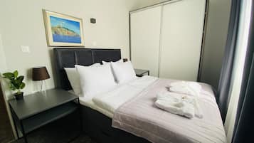 A hotel room with a bed, a nightstand, a lamp, a potted plant, and a painting on the wall.