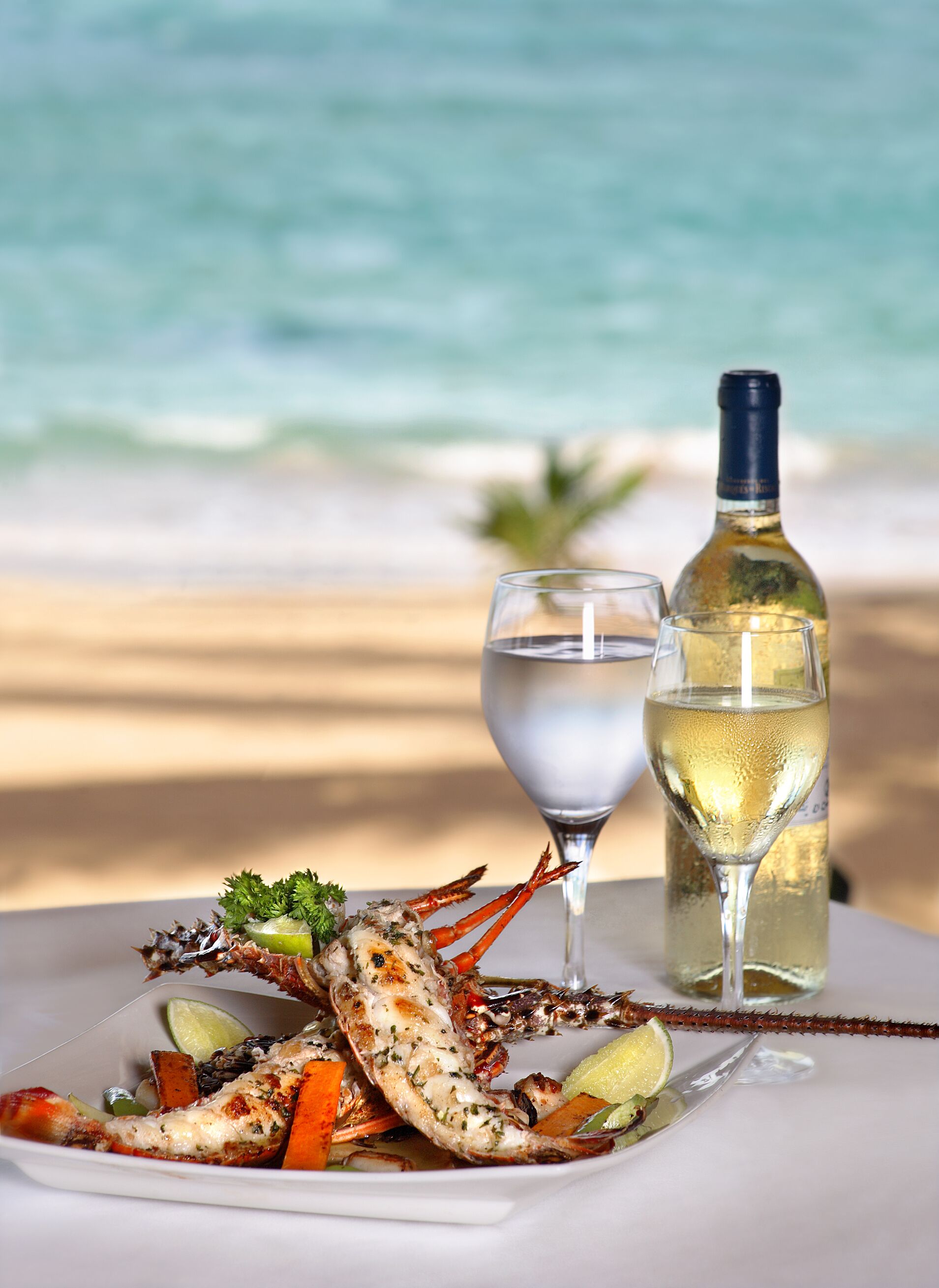 Plato de mariscos con una copa de vino blanco y una botella sobre una mesa cerca de la playa.