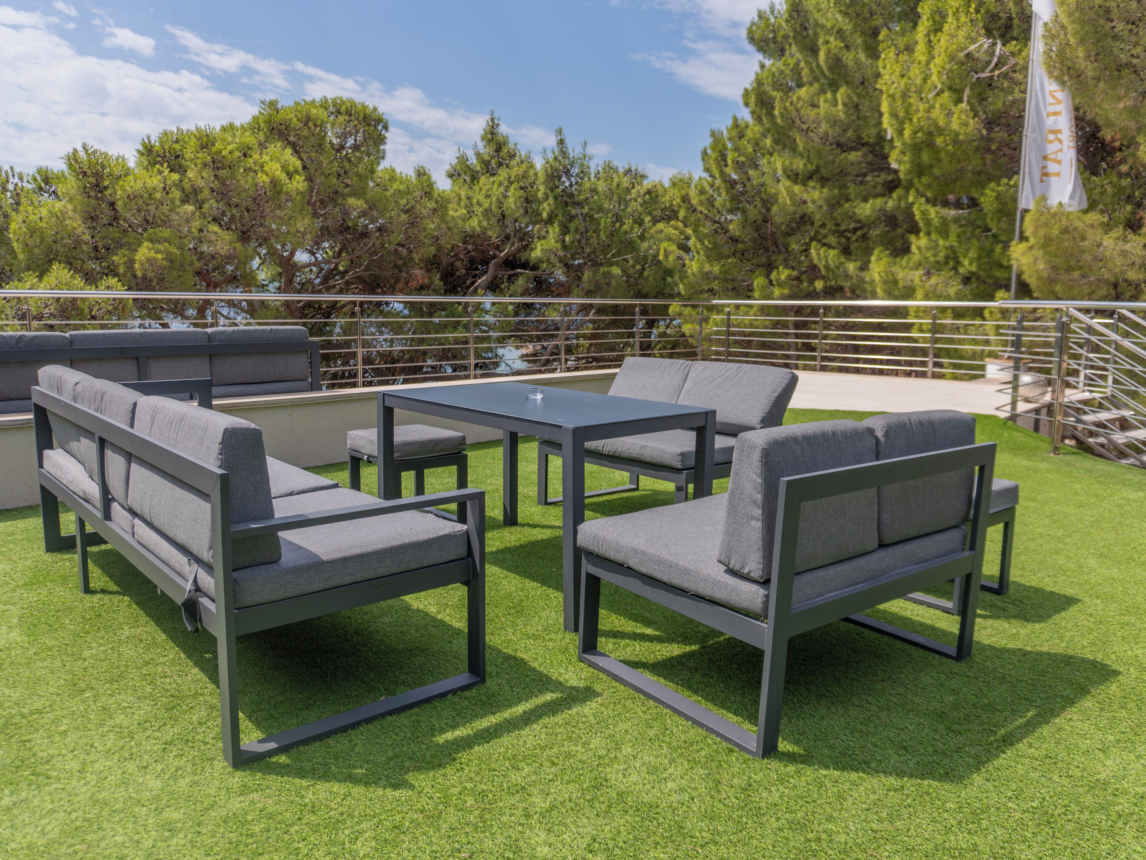 An outdoor seating area with a table and chairs, surrounded by a railing and trees.