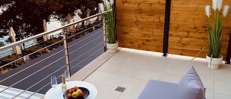 An outdoor seating area with a sofa, a small table with a bowl of fruit and glasses, and a wooden fence.