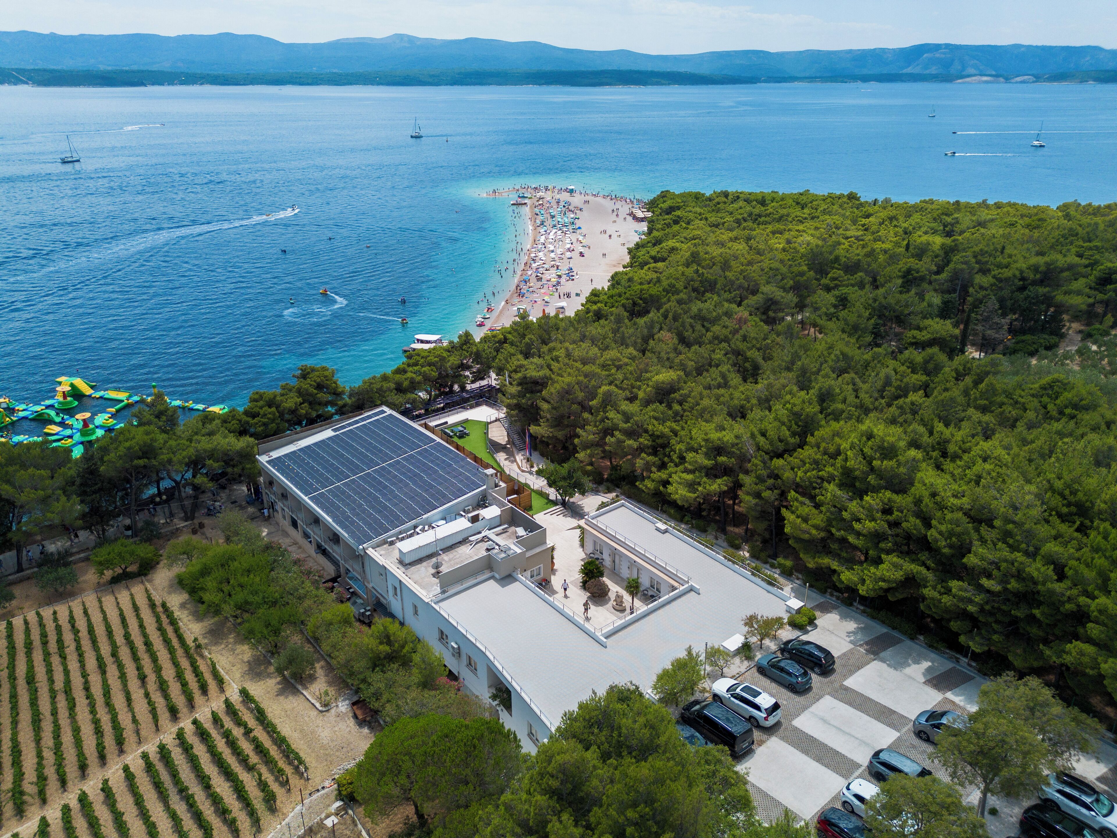 An aerial view of a coastal property with a beach, a parking area, and a building with a solar panel.
