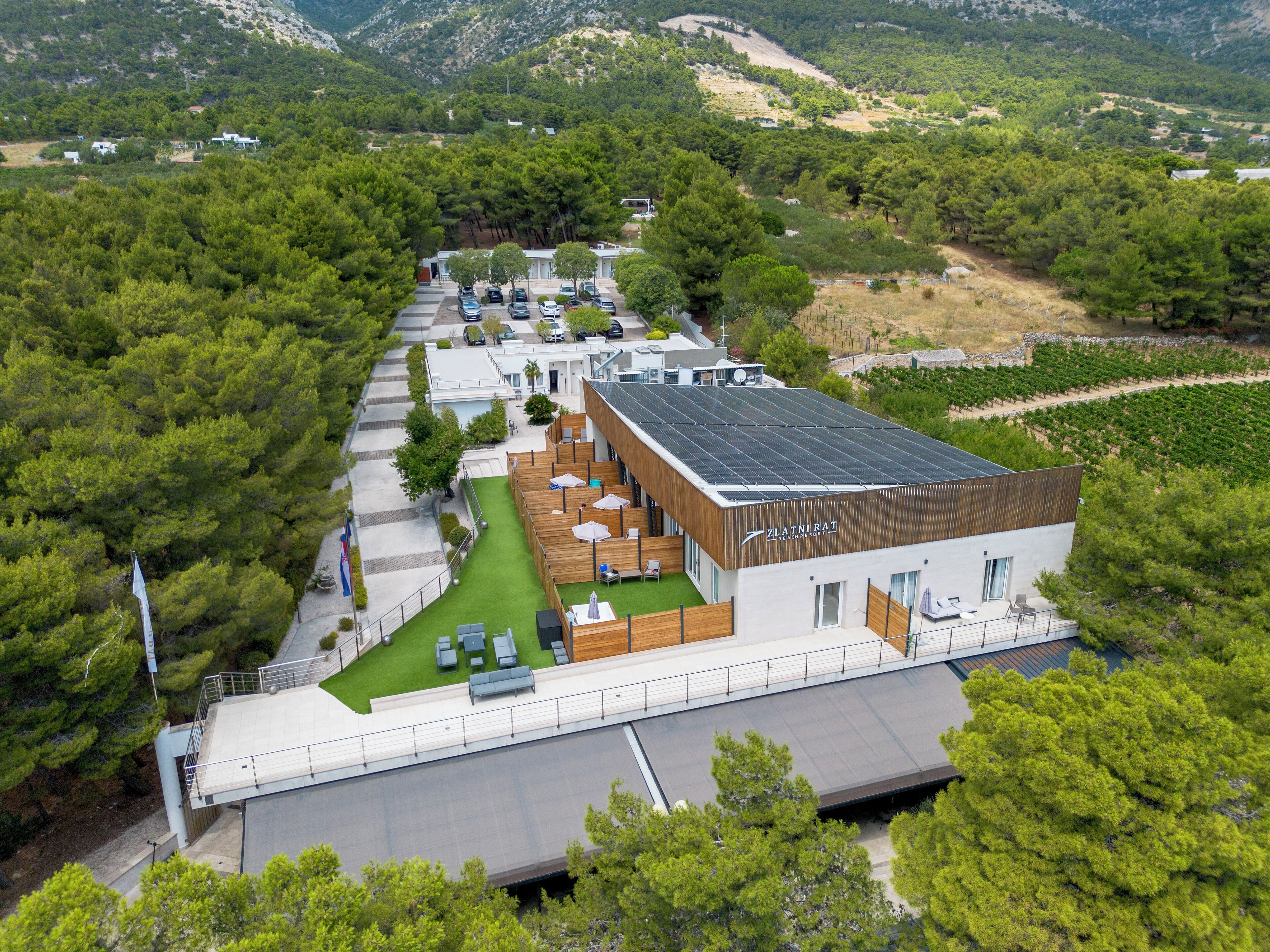 A modern hotel with a rooftop terrace, surrounded by lush greenery and vineyards.