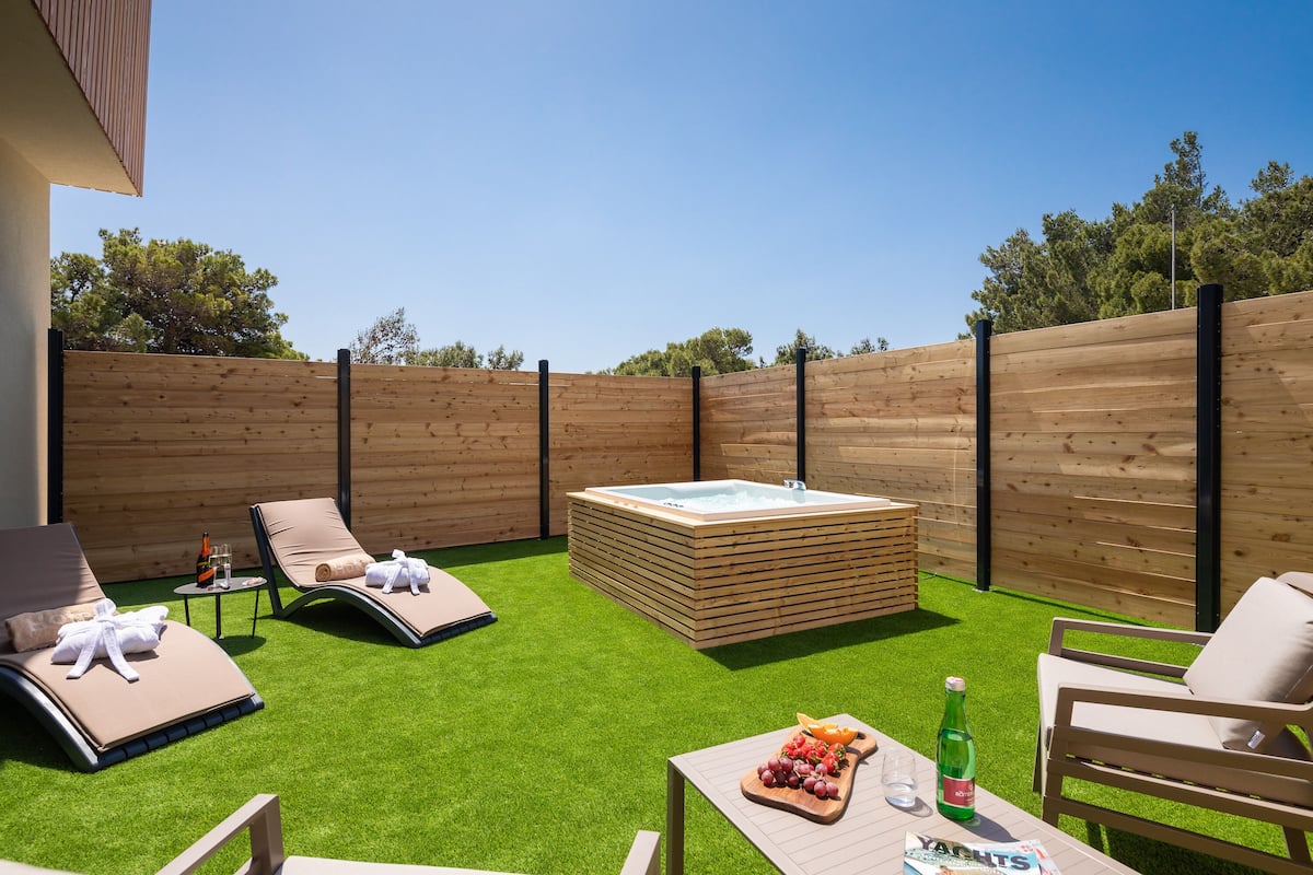 Un jardin avec une pelouse artificielle, un jacuzzi, des chaises longues et une table avec des collations et des boissons.