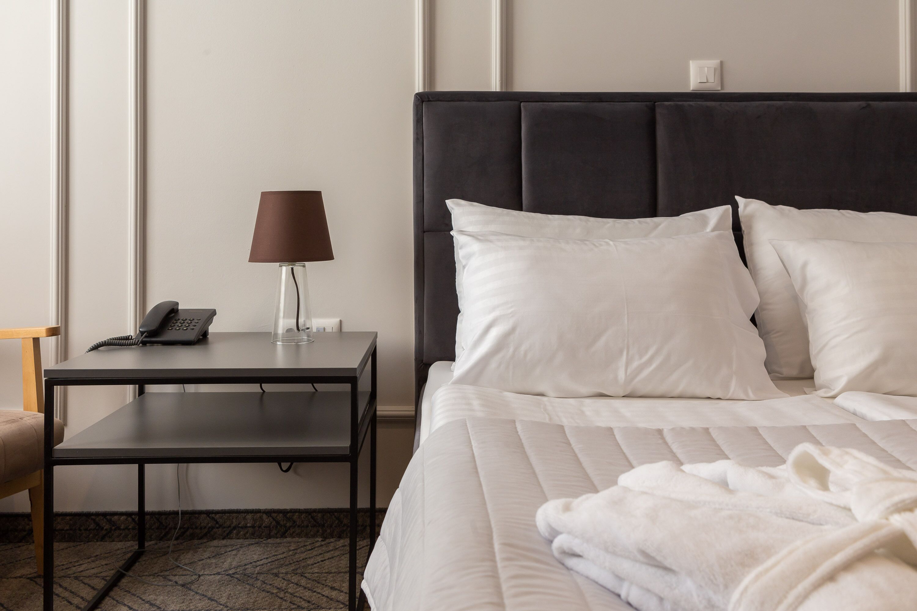 A hotel room with a bed, a bedside table with a lamp, a phone, and a chair.