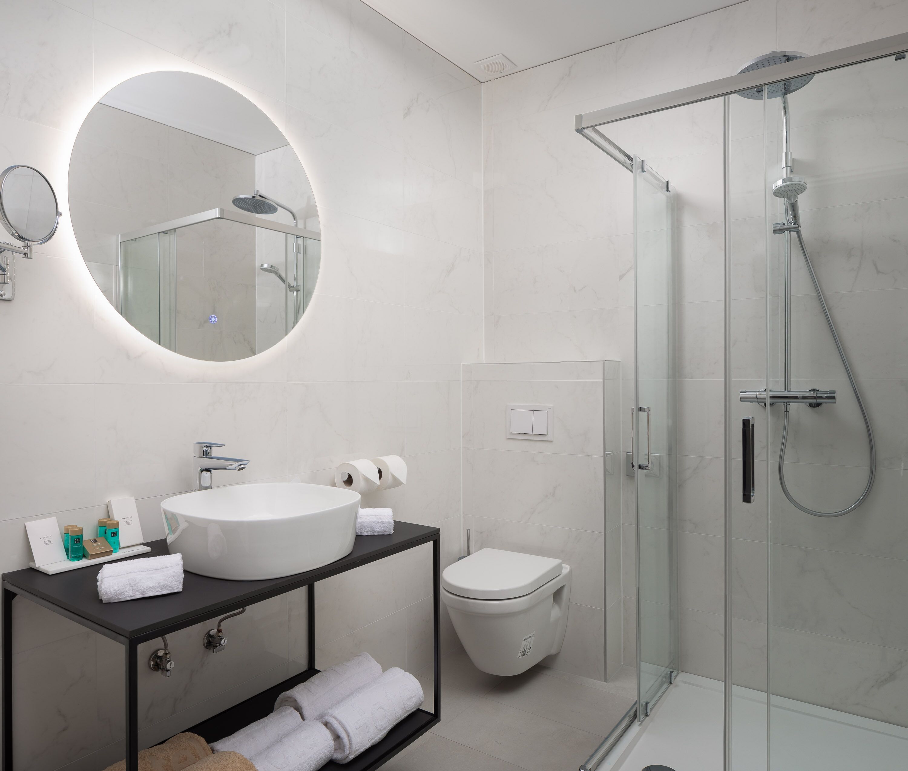 A modern bathroom with a round mirror, a sink, a toilet, and a glass-enclosed shower.