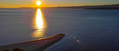 A sunset over a calm body of water with a road curving along the shore.