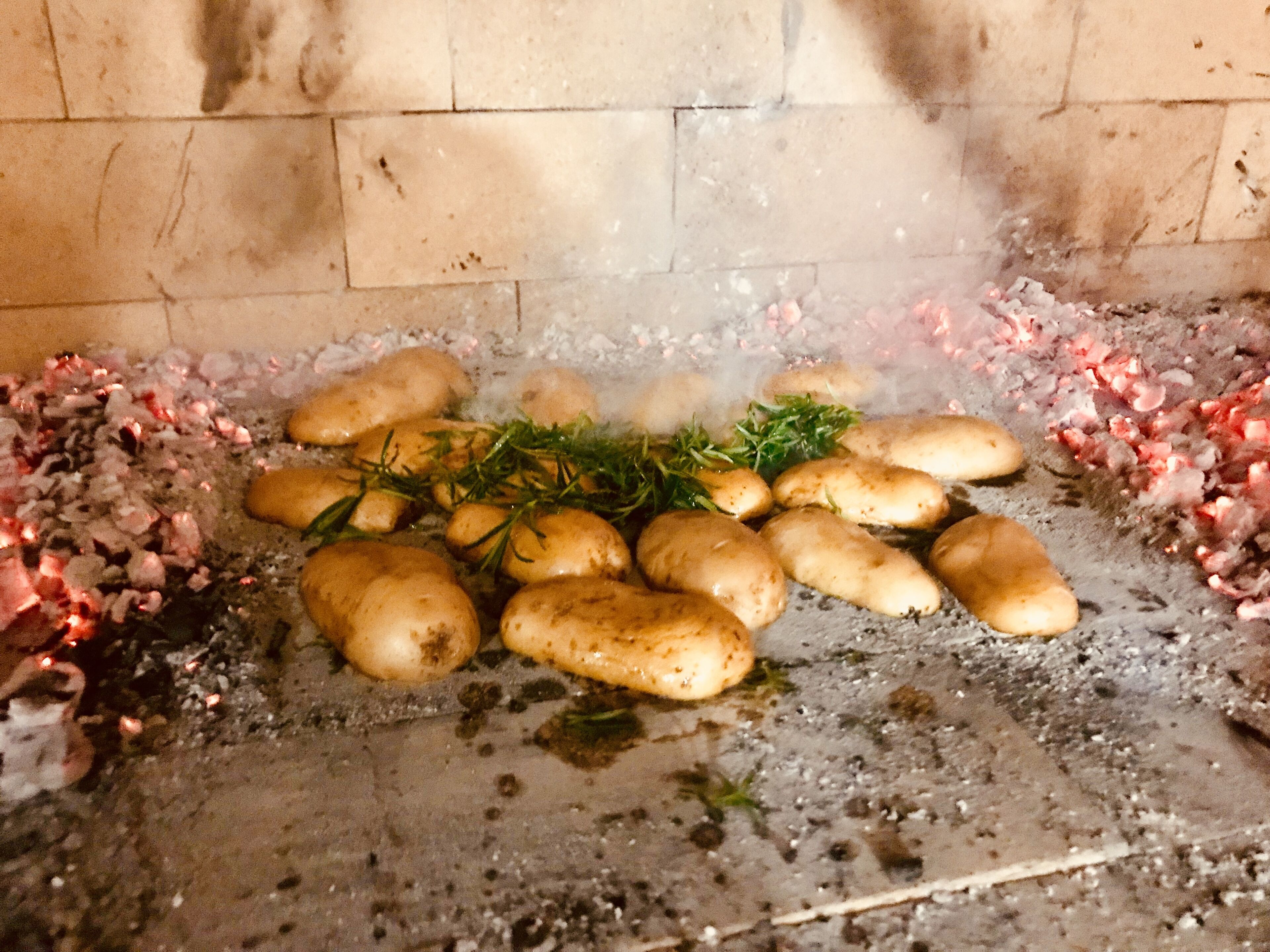 Potatoes cooking on a stove with a brick wall in the background.