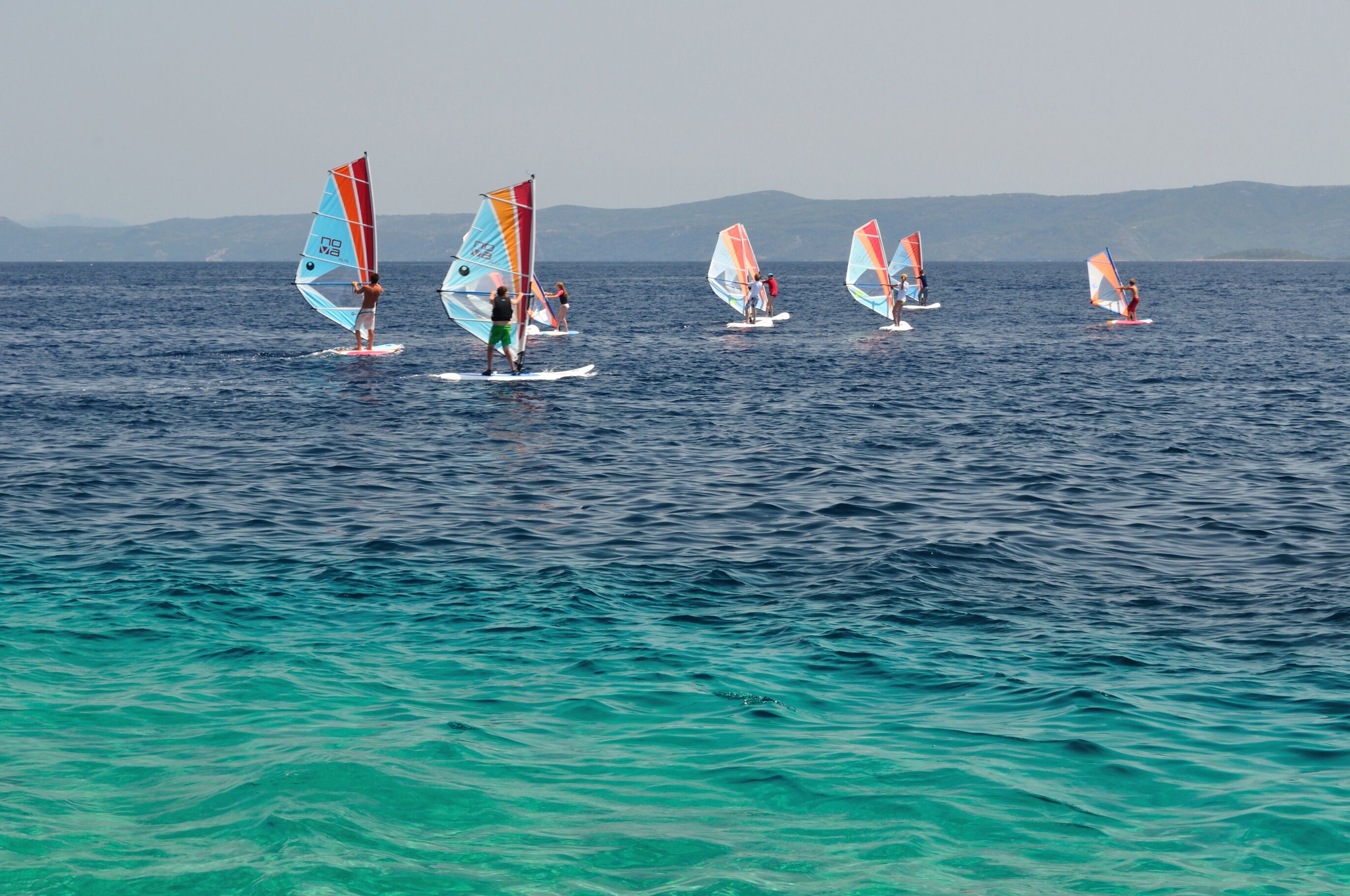 A group of people windsurfing on a calm sea with mountains in the background.
