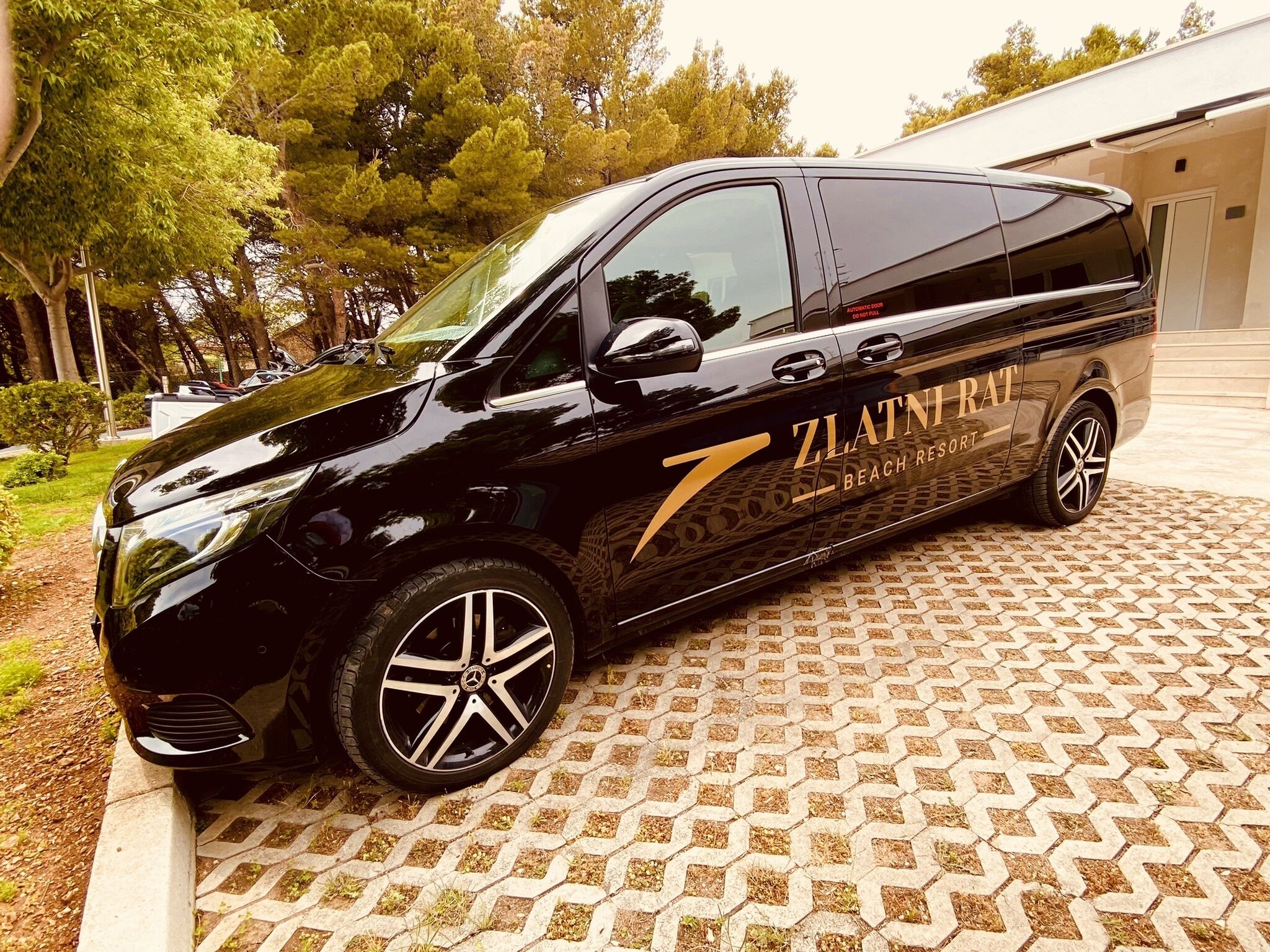 Una camioneta negra estacionada sobre un pavimento estampado, con el texto "ZLATNIRAT BEACH RESORT" en su lateral.