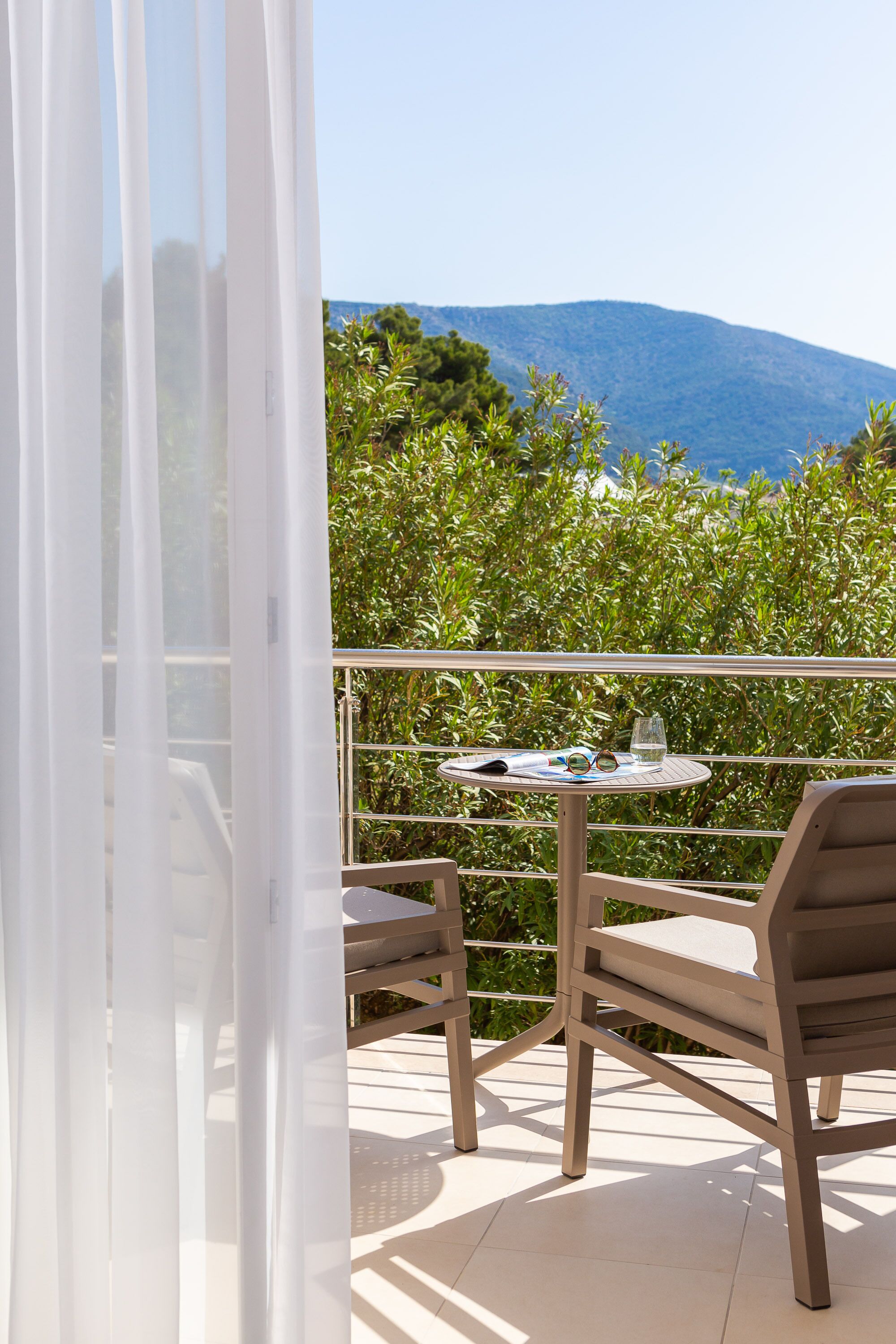 A balcony with a table and chairs, a glass of water, and a pair of sunglasses.