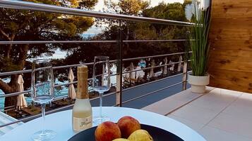 Una mesa con un cuenco de fruta y una botella de champán en un balcón con vistas a una piscina.