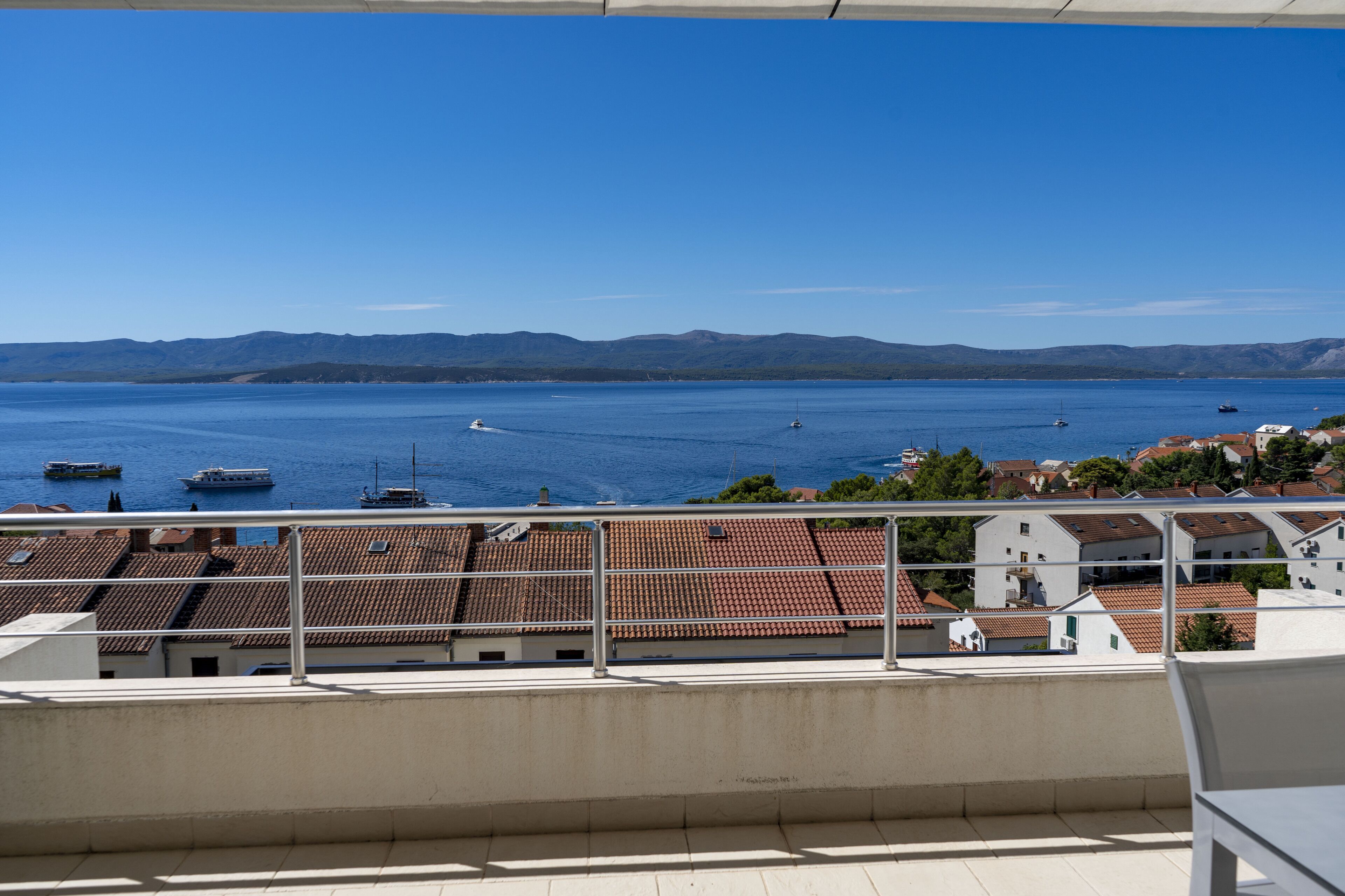 A balcony with a view of a calm sea and distant mountains.
