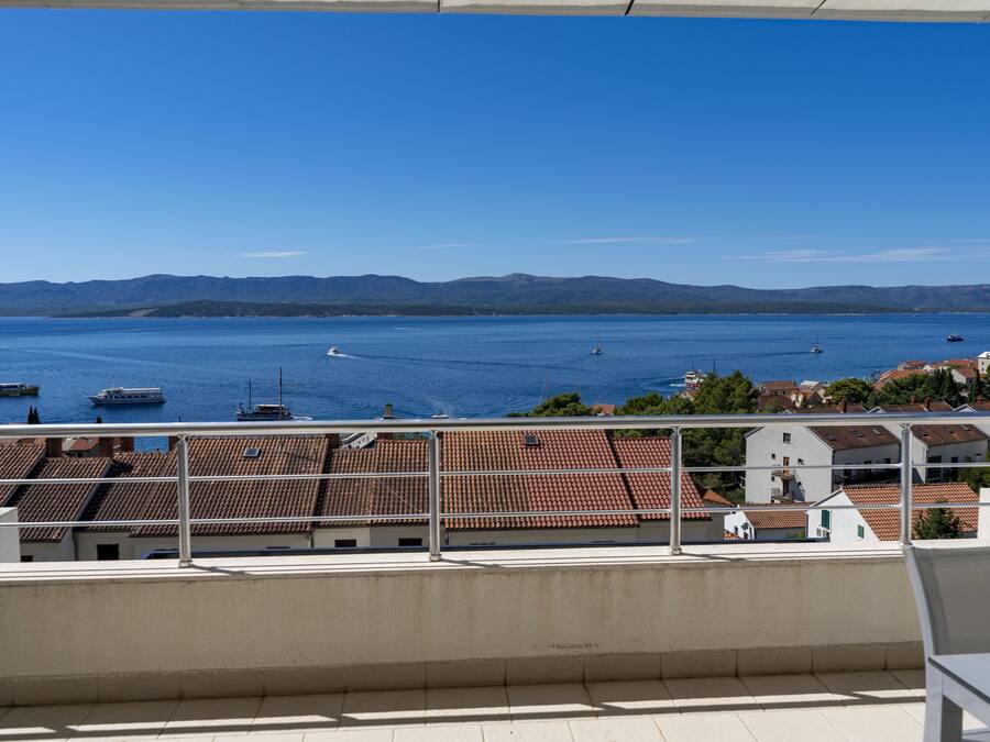 A balcony with a view of a calm sea and distant mountains.