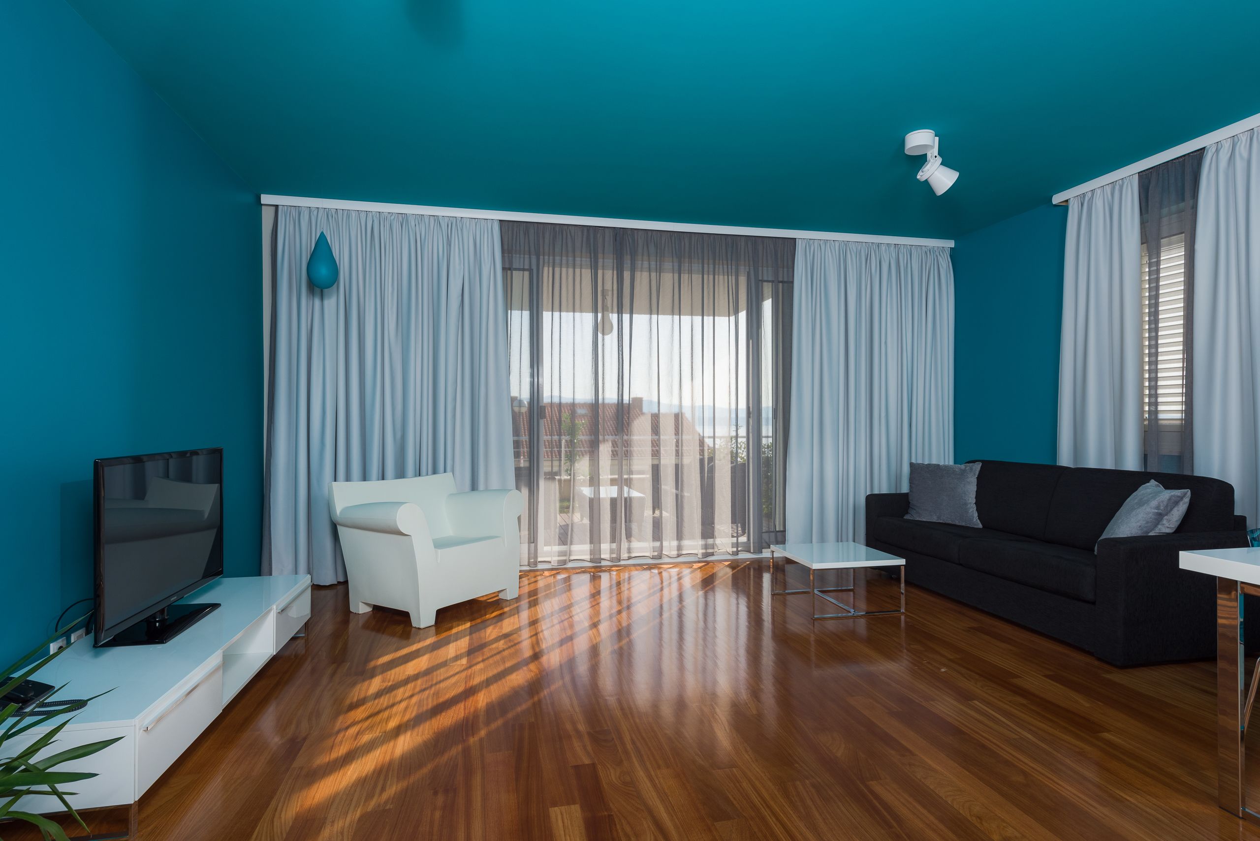 A modern living room with a flat-screen TV, a white sofa, a black sofa, and a glass door leading to a balcony.