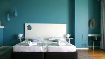 A modern bedroom with teal walls, a large bed with white bedding, two bedside tables with lamps, and a round mirror on the wall.