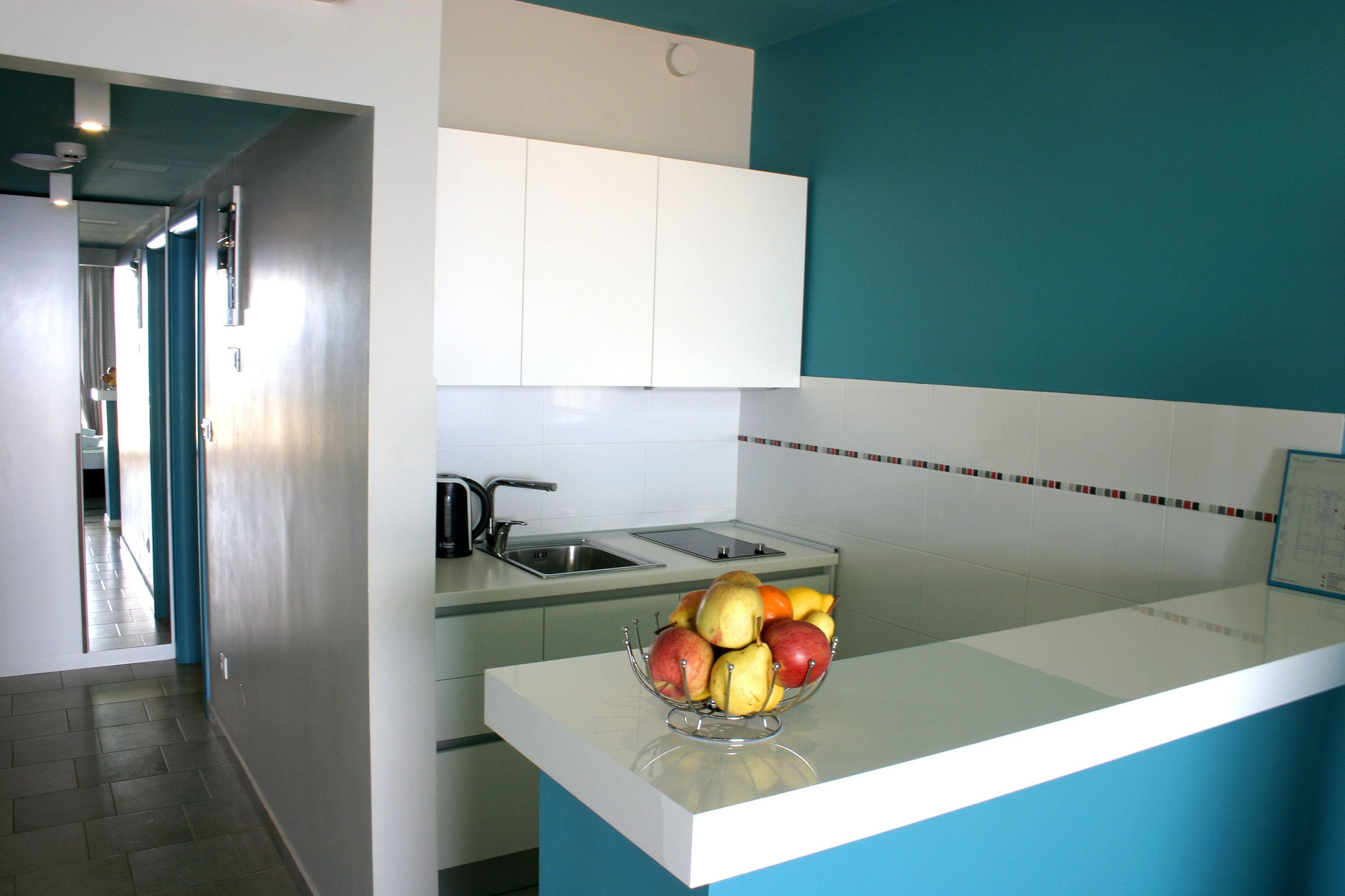 A modern kitchen with white cabinets, a blue accent wall, and a fruit bowl on the counter.
