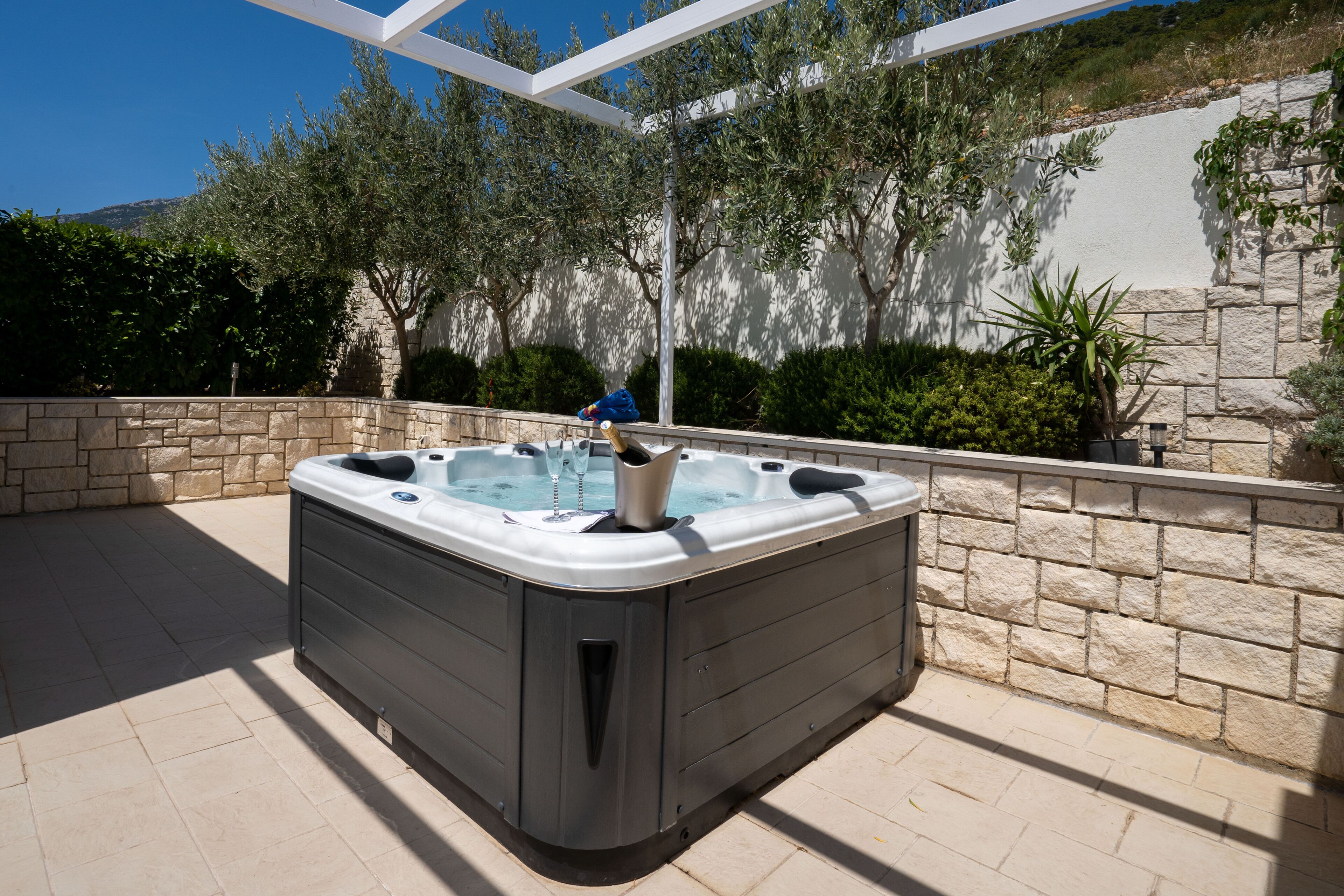 A hot tub in an outdoor setting with stone walls and greenery.