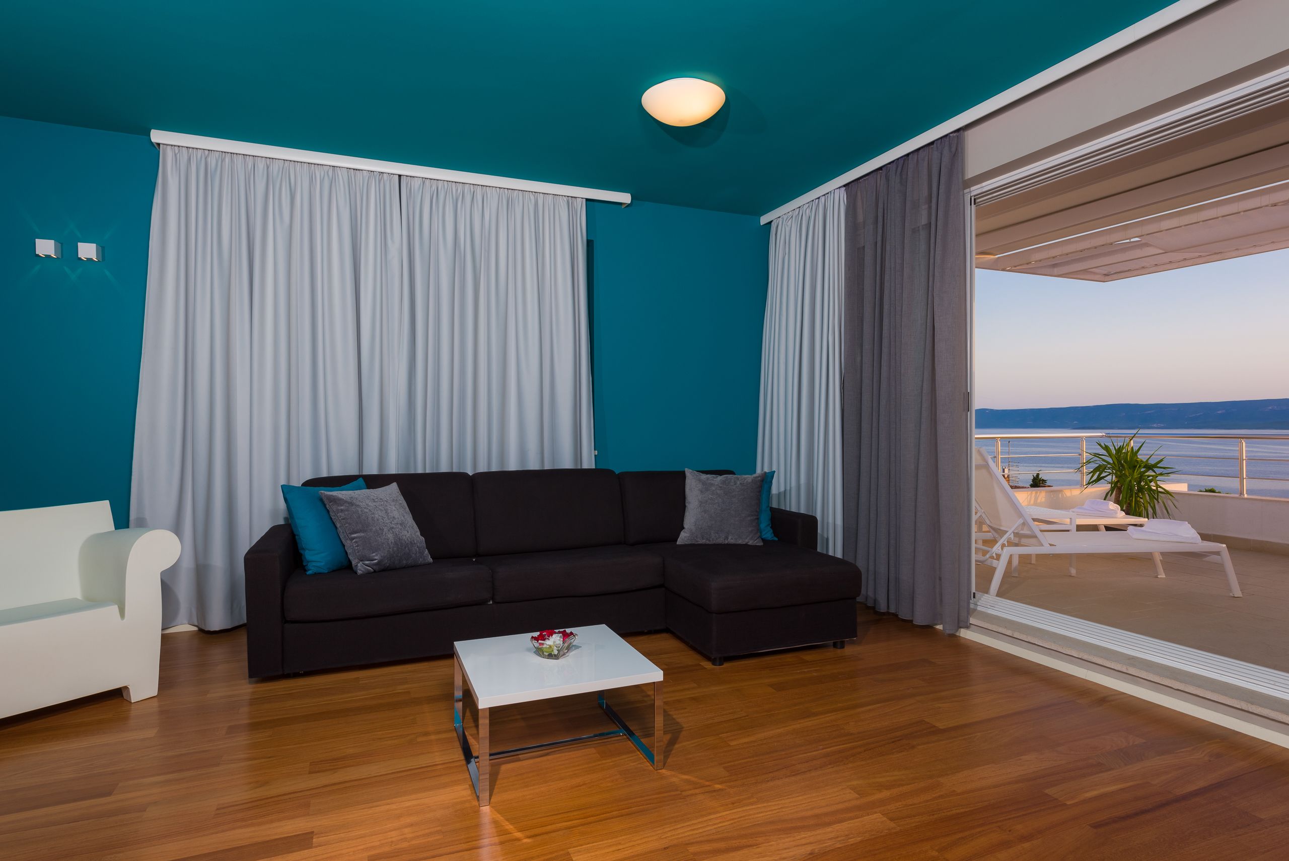 A modern living room with a black sectional sofa, a white coffee table, and a view of the sea through large windows.
