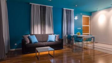 A modern living room with a dark sofa, a small table, and a dining area with a table and chairs.